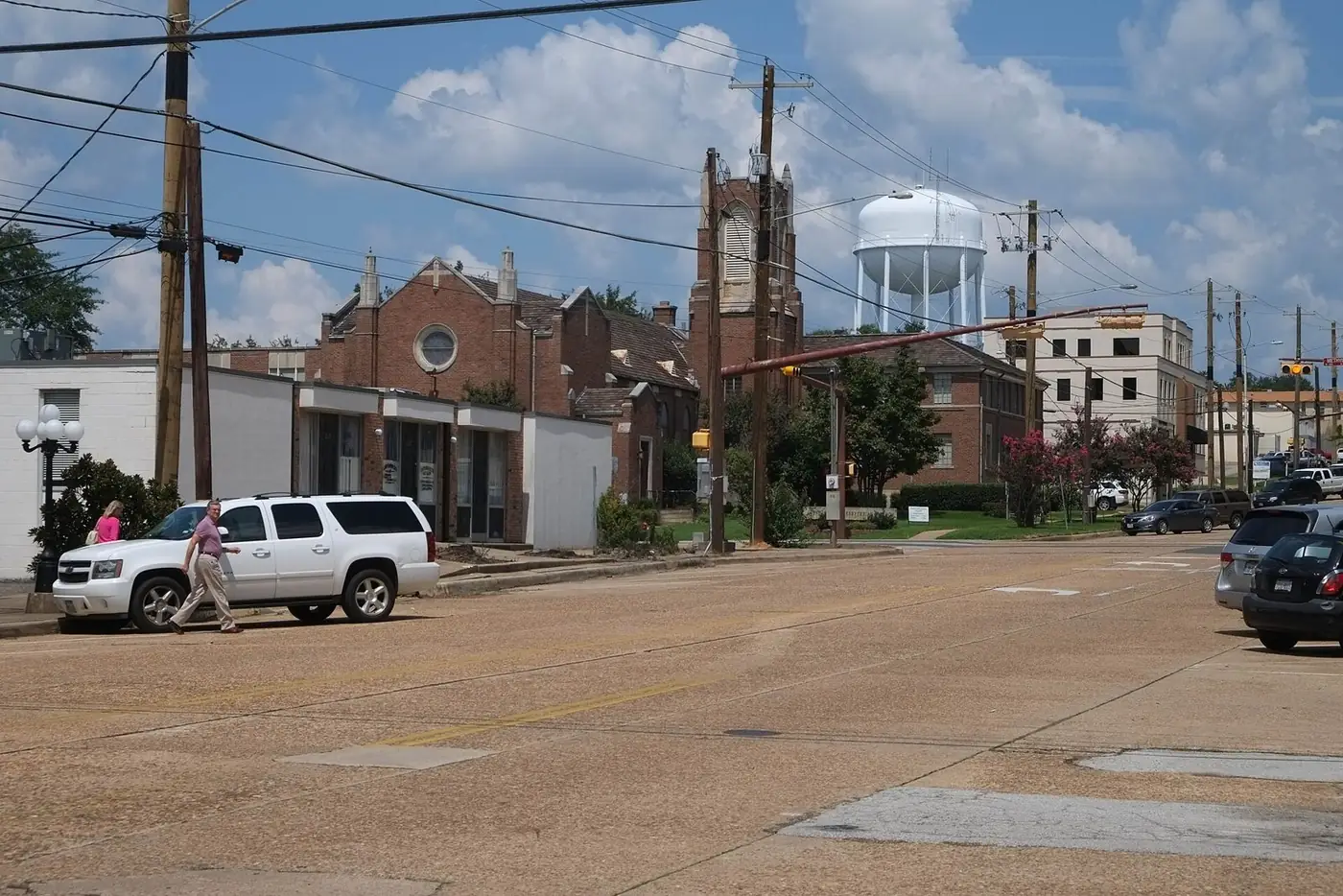 A downtown Longview street with brick buildings, a church tower and a white water tower under a cloudy sky